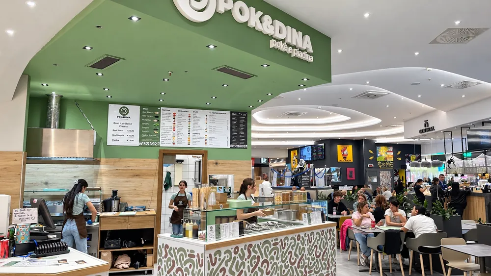 Il bancone di POK&DINA nell'area ristorazione del centro commerciale Tanit, con l'insegna verde e il menu